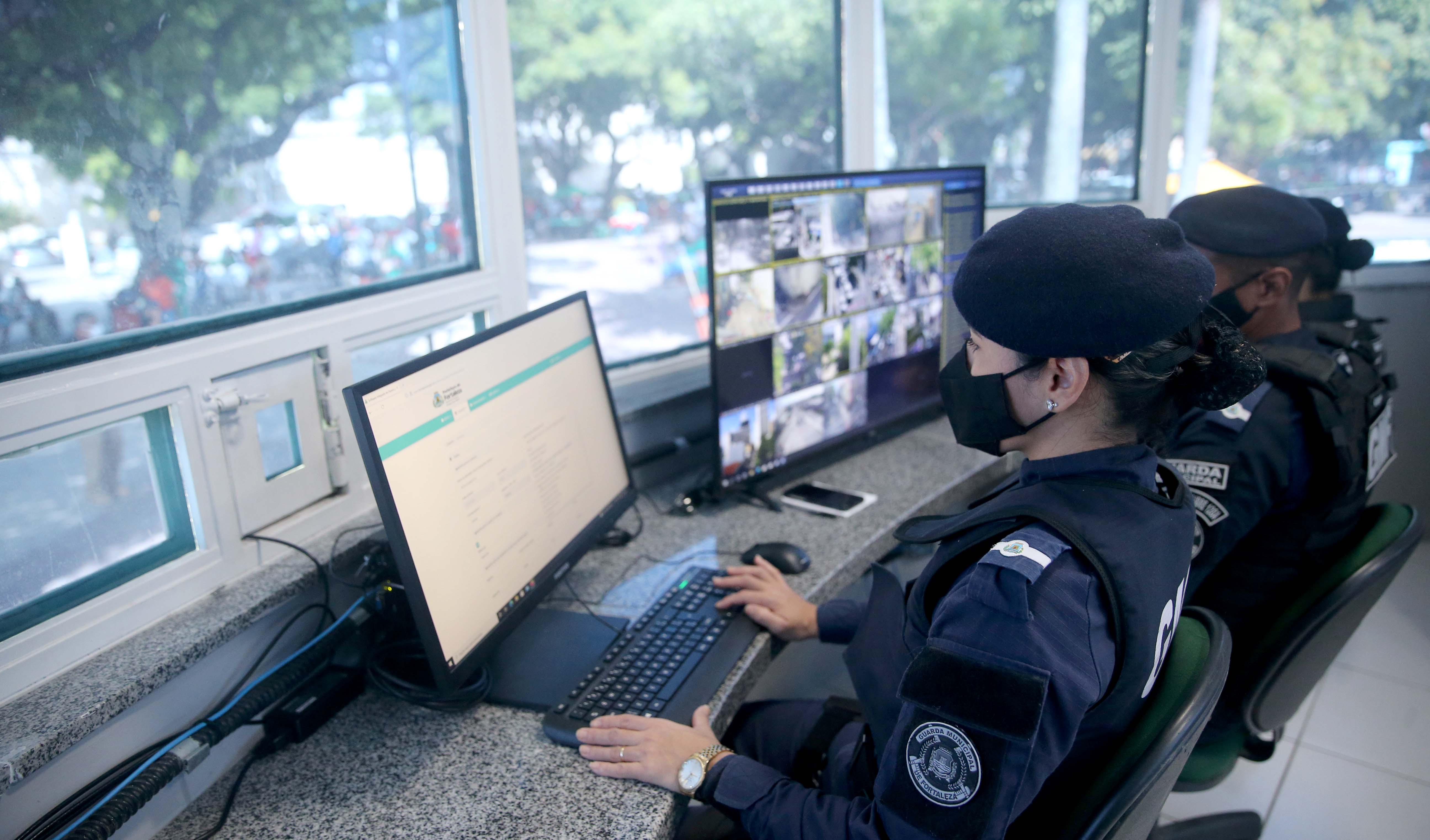 duas guardas municipais de máscara olham os monitores dentro da célula proteção comunitária